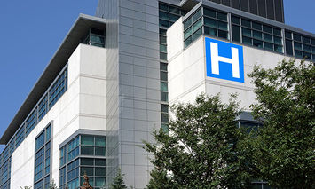 A multi-story hospital building displays a large blue 